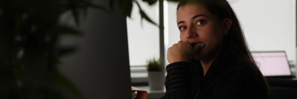 Mulher em um escritório com iluminação baixa, sentada diante do computador e observando a tela com expressão atenta e cautelosa, ilustrando o tema **como identificar phishing por e-mail** ao representar o momento de análise crítica de mensagens suspeitas, reforçando a necessidade de verificar remetentes, links e possíveis sinais de fraude antes de qualquer ação.